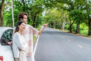 Young asian couple get out of the car and walk to enjoying the view, standing near the car, Man and woman looking at sunset and beautiful nature, Boy and girl standing by the machine photo