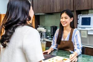 Smiling young asian waitress in a cafe with customer for service, payment or order on counter at coffee shop. Serving, employee in small business restaurant helping a girl client at checkout or work photo