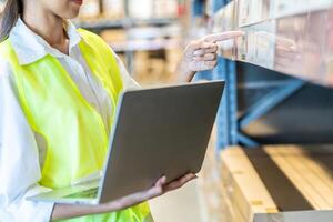 Portrait of asian woman warehouse worker in uniform checks stock and inventory with digital laptop computer, working in delivery, distribution center, logistic and business export photo