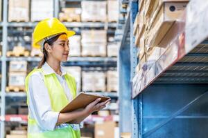 Asian woman warehouse worker in uniform doing stocktaking of products management in cardboard box on shelves in warehouse using clipboard file and pen, logistic and business export photo