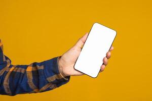 Technology, communication, and advertising concept. Close-up of hand holding a mobile phone with blank copy space screen for text message or information while standing with a yellow background photo