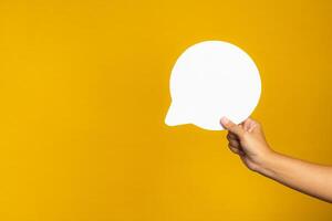 A speech bubble concept. Hand holding of an empty white speech balloon on yellow background with copy space for text photo