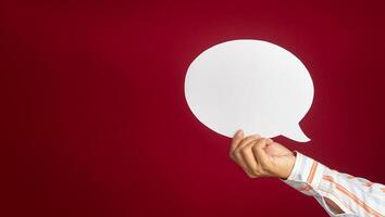 A speech bubble concept. Hand holding an empty white speech bubble over on a red background with copy space for text photo