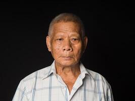 Portrait of an elderly Asian man in a white shirt looking at the camera with a smile while standing on a black background in the studio photo
