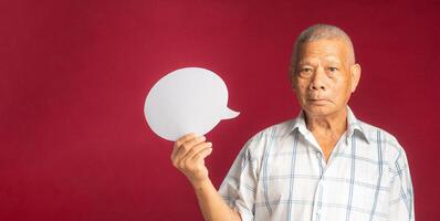 Portrait of a senior man holding a blank paper speech bubble and looking at the camera with a smile while standing on a red background photo