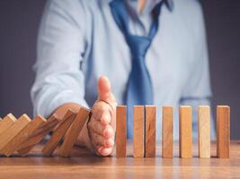 Risk management concept. Close-up of hand businessman stopping the domino business crisis effect before the business collapse. Business crisis management conceptual photo