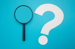Search and question mark concept. A magnifying glass and a white question mark symbol are on a blue background. Top view. Space for text photo