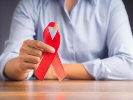 Red ribbon awareness concept. Woman in a blue shirt with hand holding a red ribbon while sitting in the office. World AIDS day, World cancer day, World hypertension day. Space for text photo