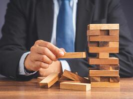 Risk of management and strategy plans for business growth and success concept. Close-up hand of the businessman in a suit playing a wooden block game while sitting at the work table. Space for text photo