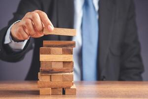 Risk of management and strategy plans for business growth and success concept. Close-up hand of the businessman in a suit playing a wooden block game while sitting at the work table. Space for text photo