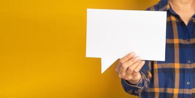 Business and speech bubble concept. Businessman in a blue shirt holding an empty speech bubble paper while standing on a yellow background in the studio. Space for text. Close-up photo