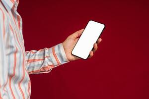 Technology, communication, and advertising concept. Close-up of hand holding a smartphone with blank copy space screen for text message or information while standing with a red background photo