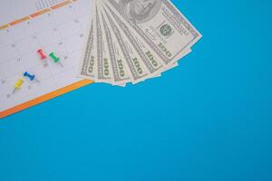 A calendar page date and US dollar banknotes are isolated on blue background. Appointment schedule. Top View. Space for text. Business and finance concept photo