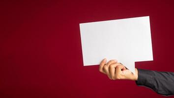 A speech bubble concept. Hand holding an empty white speech bubble over on a red background with copy space for text. Close-up photo