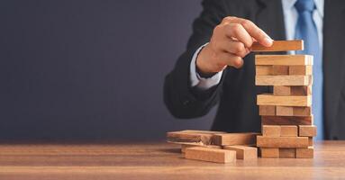 Risk of management and strategy plans for business growth and success concept. Close-up hand of the businessman in a suit playing a wooden block game while sitting at the work table. Space for text photo