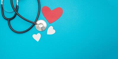 Top view of a stethoscope with red and white heart paper shape on a blue background. Space for text. Medical and healthcare concept photo