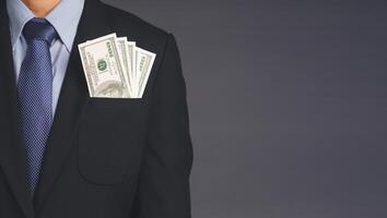 Business, finance, payday loan concept. Businessman wearing a suit with US dollar banknotes in a suit pocket while standing with a gray background with space for text photo
