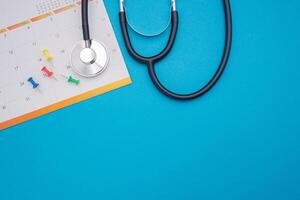 A stethoscope and calendar page date isolated on blue background. Doctor appointment schedule. Top View. Space for text photo