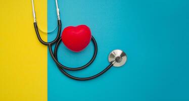 Top view of a stethoscope and a red heart shape on a yellow and blue background. Space for text. Medical and healthcare concept photo