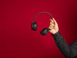 Hand holding a wireless headphone over a red background with copy space for text. Close-up photo. Music and relaxation concept photo