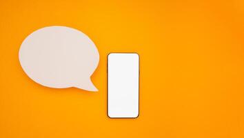 Top view of a blank white speech bubble and a mobile phone isolated on a yellow background. Phone message. Advertisement idea. Empty speech balloon for advertising photo