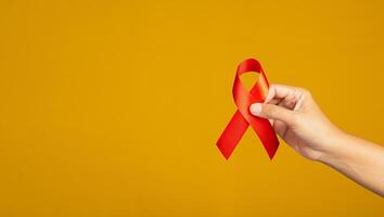 Red ribbon awareness concept. Close-up of hand holding a red ribbon over yellow background. World AIDS day, World cancer day, World hypertension day. Space for text photo
