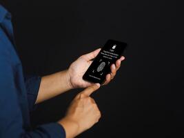 Young man scanning fingerprint biometric identity and approval on a smartphone while standing on a gray background. Business technology safety internet and biometric security Concept photo