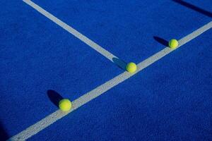 Three paddle tennis balls on the line of a blue paddle tennis court. photo
