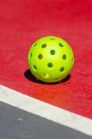 A pickleball ball in a red and grey court, defocused background. Racket sport photo