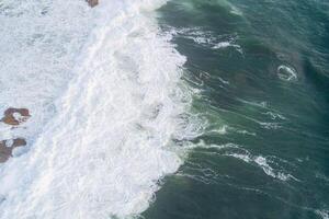 Aerial photo of a rocky shore with crashing waves creating foam.