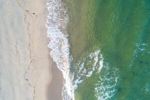 Beach sand sea shore with green wave and white foamy summer background. Overhead drone view photo