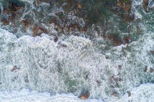 Aerial photo of a rocky shore with crashing waves breaking and creating foam.