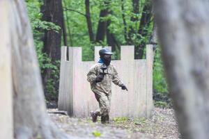 Paintball game. Players with weapons shooting paint balls. Men on the playground. Guys in camouflage and masks are fighting. photo