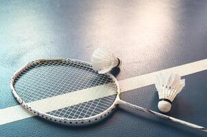 Cream white badminton shuttlecock and racket with neon light shading on dark floor in indoor badminton court, copy space, soft and selective focus. photo
