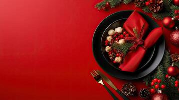 A festive Christmas table setting with black plates, red napkins, and holiday greenery on a red background, creating a luxurious holiday ambiance. photo