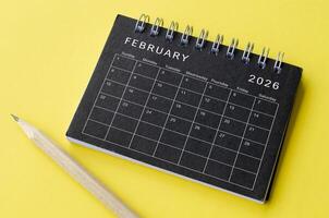 Top view of February 2026 calendar on black notepad with yellow background photo