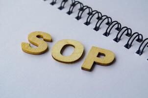 Top view of SOP wooden letters on white notepad. Standard Operating Procedure concept photo