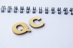 Top view of QC wooden letters on white notepad. QC for Quality Control photo