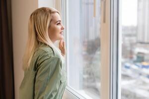Young woman is standing and looking out the window photo