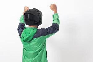 Back view of Asian online courier driver wearing green jacket and helmet raising his fist, celebrating success. Isolated image on white background photo