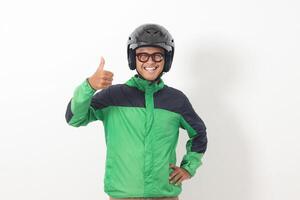 Portrait of funny Asian online taxi driver wearing green jacket and helmet showing thumb up hand gesture. Isolated image on white background photo