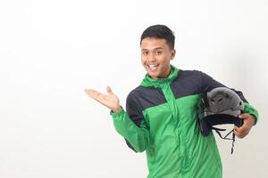 Portrait of Asian online taxi driver wearing green standing against white background, holding his helmet on his hip while pointing to the side photo
