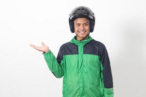 Portrait of Asian online taxi driver wearing green jacket and helmet pointing at empty space with finger. Isolated image on white background photo