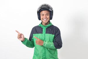 Portrait of Asian online taxi driver wearing green jacket and helmet pointing at empty space with finger. Isolated image on white background photo