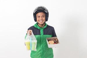 Portrait of Asian online taxi driver wearing green jacket and helmet holding a box of donuts and cup of juice drink, delivering to customer. Isolated image on white background photo