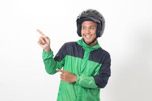 Portrait of Asian online taxi driver wearing green jacket and helmet pointing at empty space with finger. Isolated image on white background photo