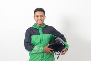 Portrait of Asian online taxi driver wearing green standing against white background, smiling and looking at camera, holding his helmet on the side photo