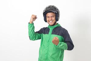 Portrait of Asian online taxi driver wearing green jacket and helmet raising his fist, celebrating success. Isolated image on white background photo