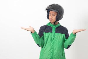 Portrait of Asian online taxi driver wearing green jacket and helmet choosing between 2 different options, holding two hands with empty space. Isolated image on white background photo