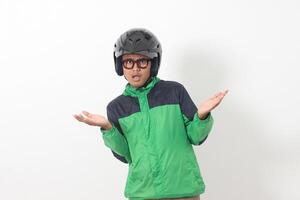 Portrait of tired Asian online taxi driver wearing green jacket and helmet doing weird funny pose. Isolated image on white background photo